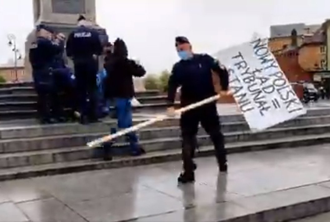 Kadr z nagrania, na którym widać jak policjanci zatrzymują mężczyznę z transparentem z napisem "Nowy Polski Ład = Trybunał Stanu".