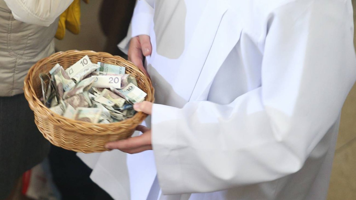Ksiądz trzymający tacę z pieniędzmi