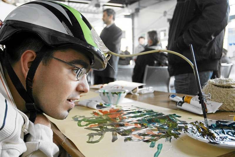 Tomek z Polskiego Stowarzyszenia na Rzecz Osób Upośledzonych Umysłowo maluje obraz za pomocą pędzli przymocowanych do kasku.