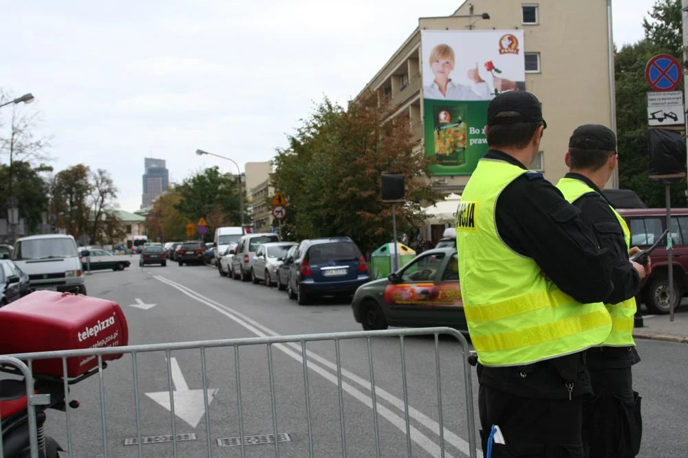 Policjanci, którzy patrzą dokładnie na zaparkowane na zakazie(!) auta. Znak w tle