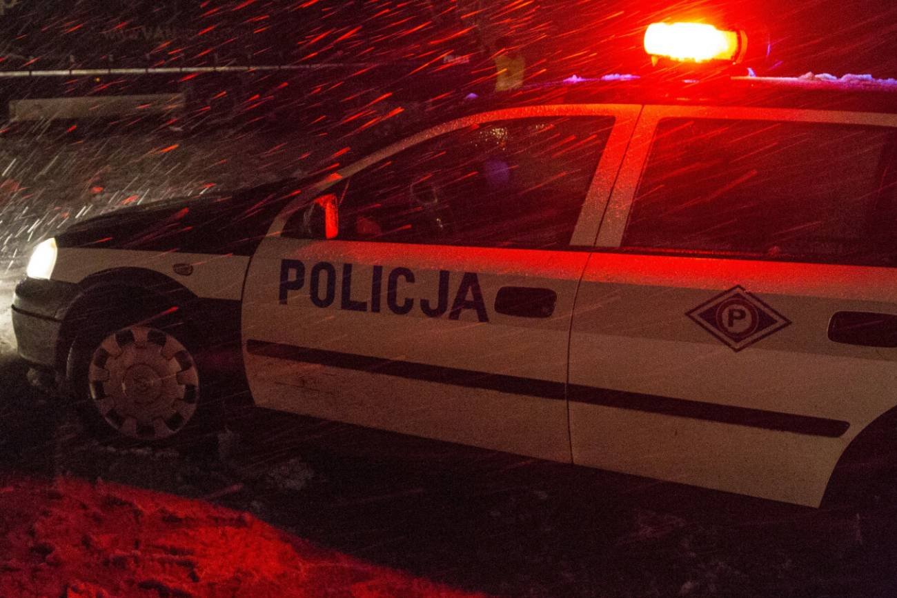 Radiowóz policyjny stojący nocą na światłach. W tle śnieżyca