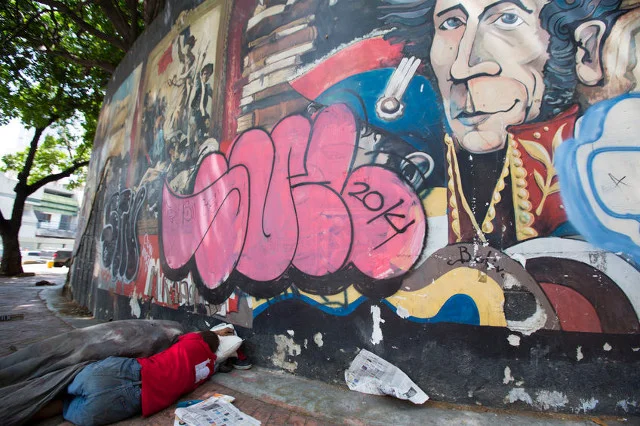 Bezdomny śpi na ulicy w centrum Caracas pod graffiti przedstawiającym Simona Bolivara.