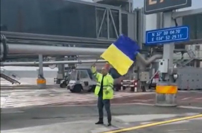 Pracownik lotniska Ben Gurion w Izraelu wymachujący flagą Ukrainy przed rosyjskim samolotem
