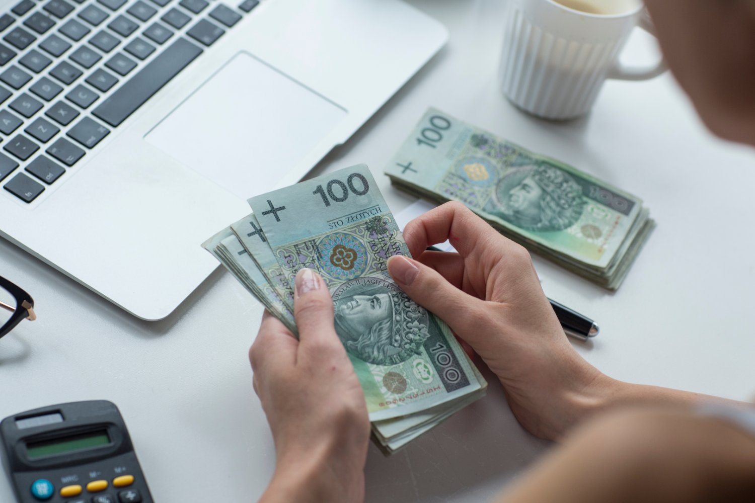 Kobieta przy laptopie licząca polskie pieniądze
