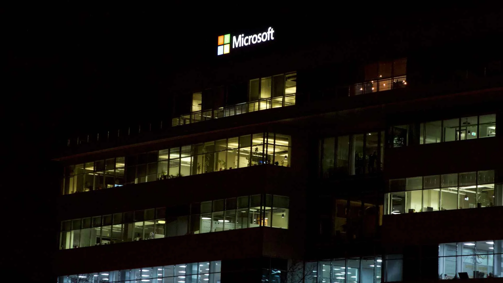 Microsoft chce zwolnić 27 proc. swojej załogi przez AI. Na razie po dobroci logo micorsoftu, budynek na nocnym tle