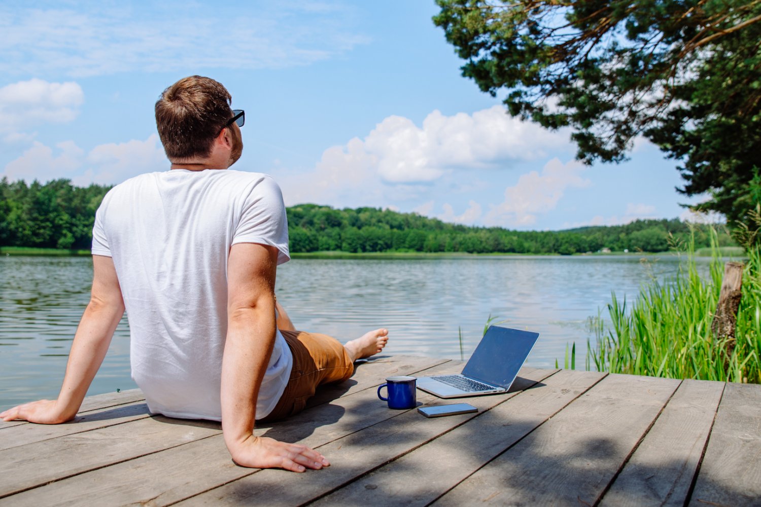 Mężczyzna przy laptopie na pomoście nad jeziorem