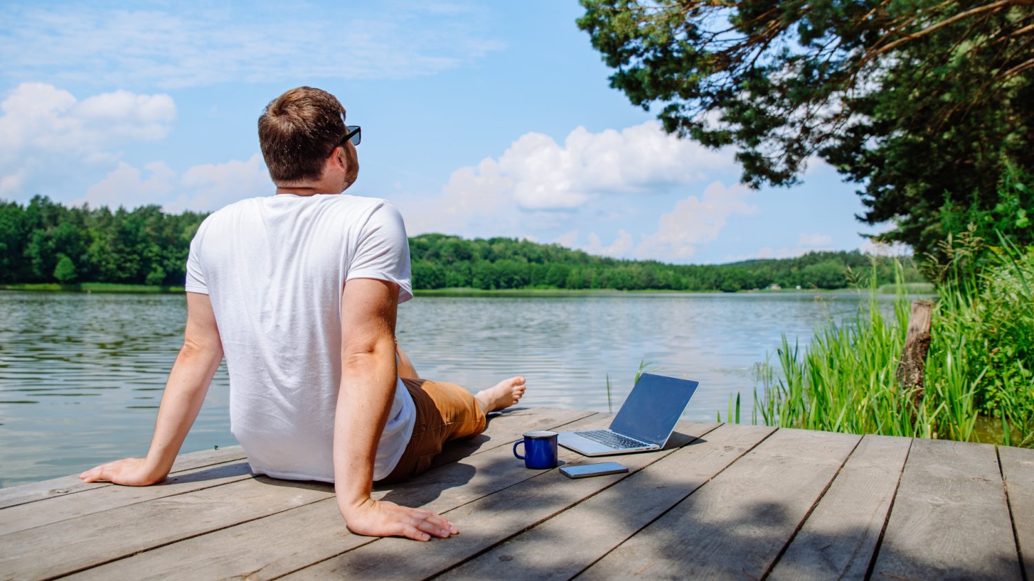 Mężczyzna przy laptopie na pomoście nad jeziorem