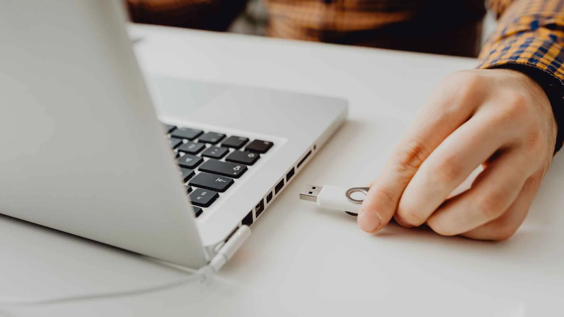 mężczyzna wypinający białego pendrive z białego komputera.