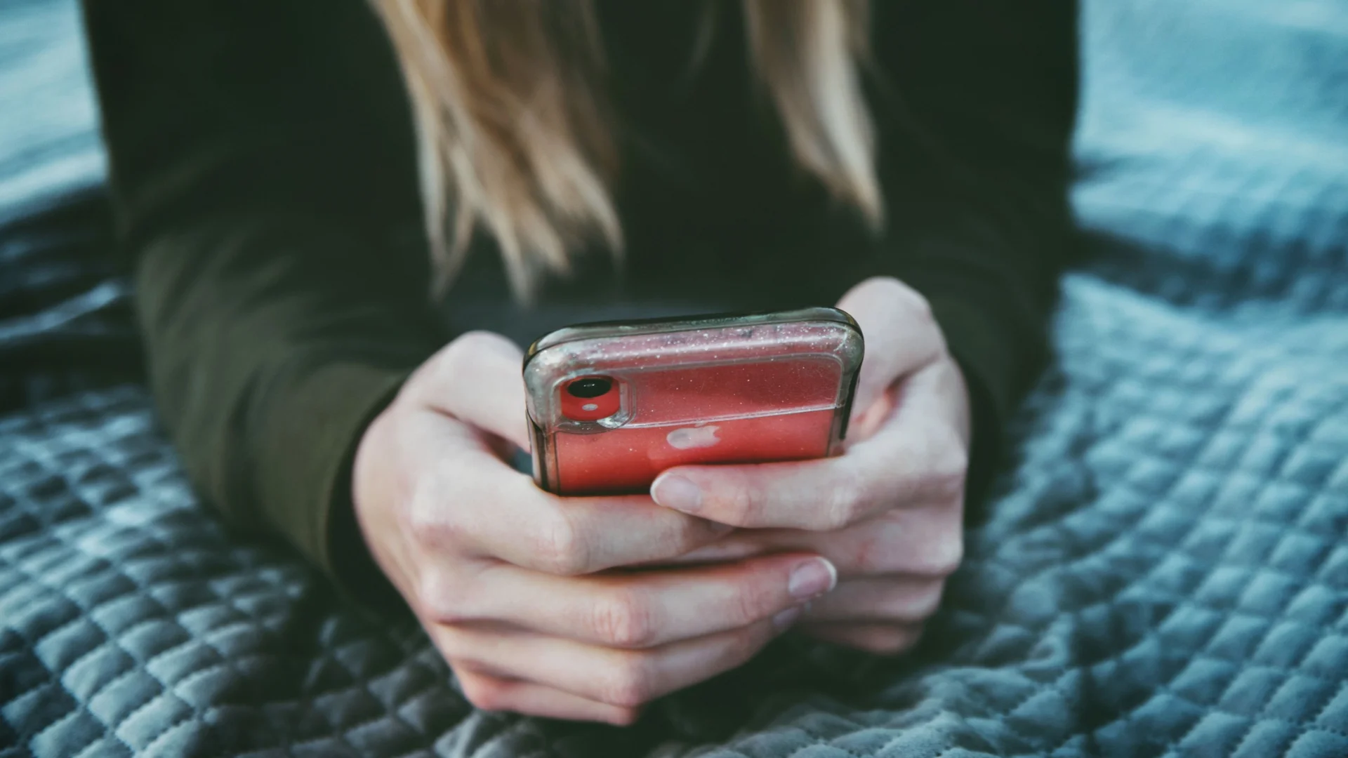 Nastolatka siedząca na łóżku i trzymająca telefon.