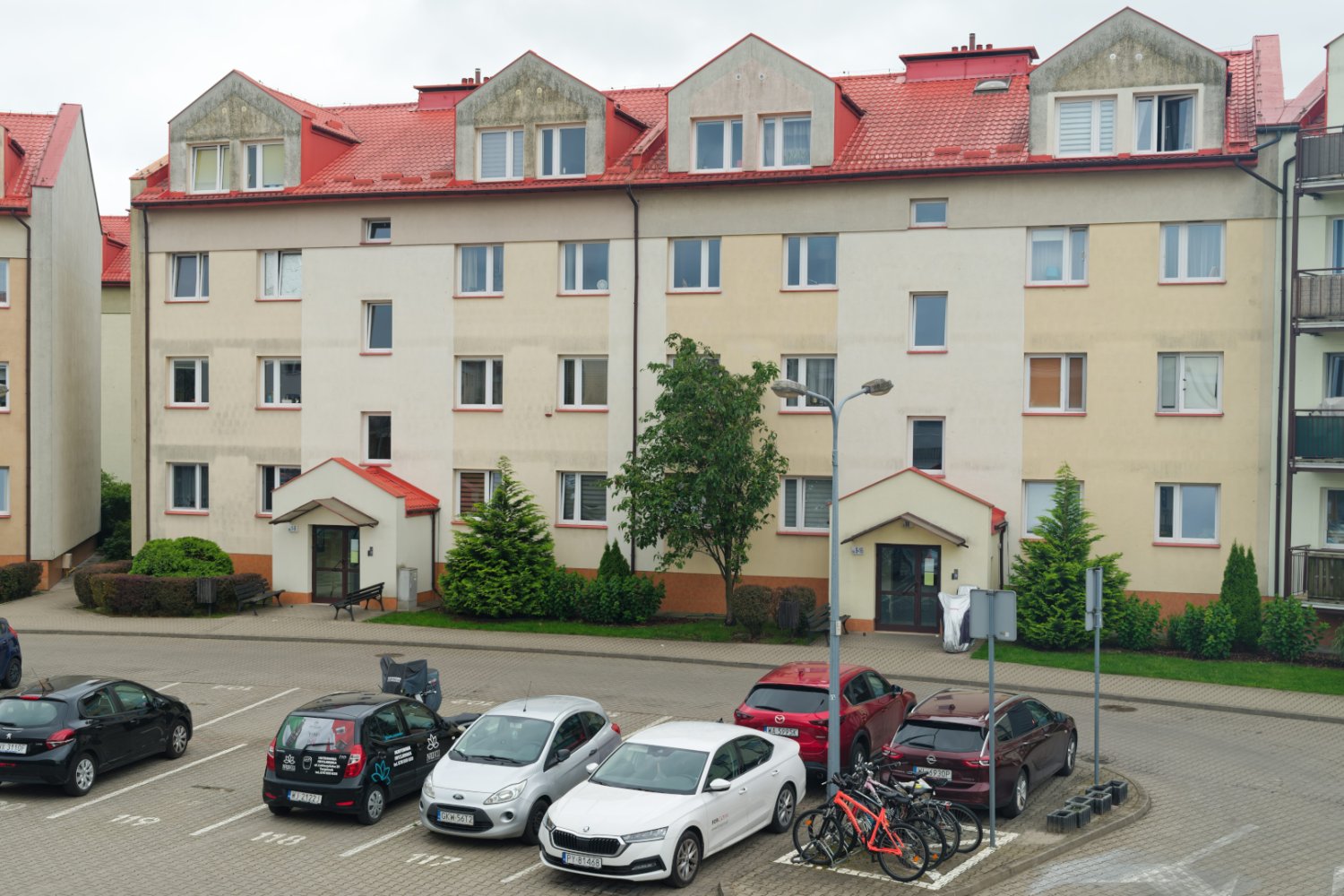 Reforma prawa budowlanego 2026. Nowe wymogi dla deweloperów Osiedle w Polsce. Parking podwórkowy obok wielopiętrowych budynków mieszkalnych z czerwonymi dachami, zaparkowanymi samochodami i roweram