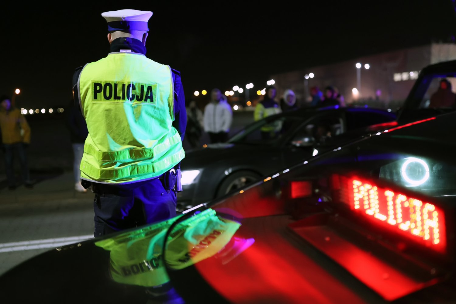 Policjant z drogówki przy radiowozie z uczestnikami nocnych wyścigów