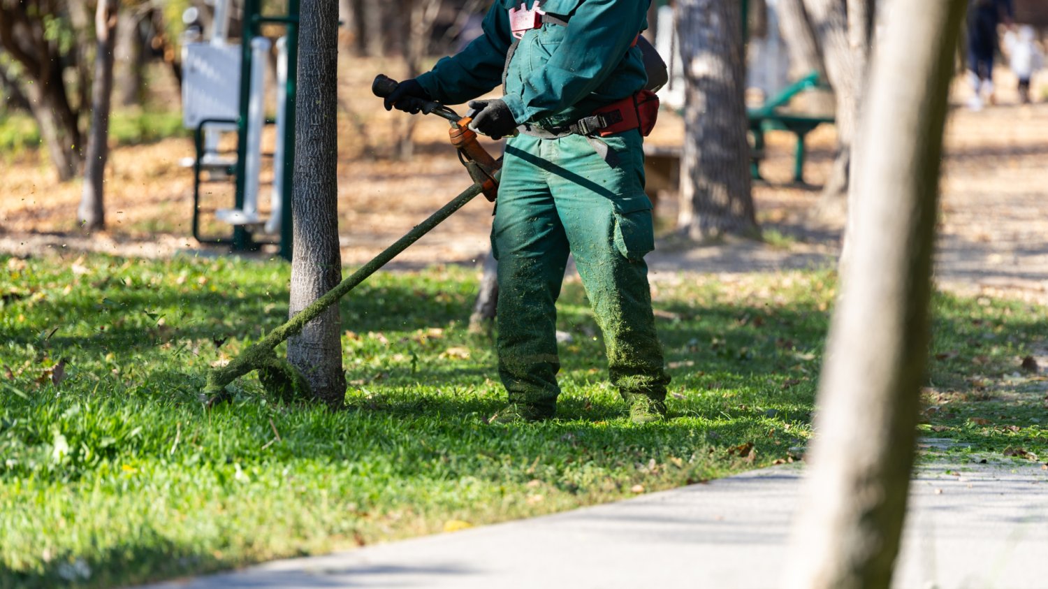 Koszenie trawy w październiku. Do kiedy można kosić? Pracownik kosi trawnik na osiedlu, jesienne koszenie trawy w mieście