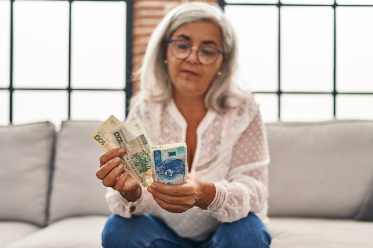 14. emerytura w 2026 roku. ZUS szykuje wypłaty, ale potrąci podatek Seniorka liczy polskie banknoty na kanapie