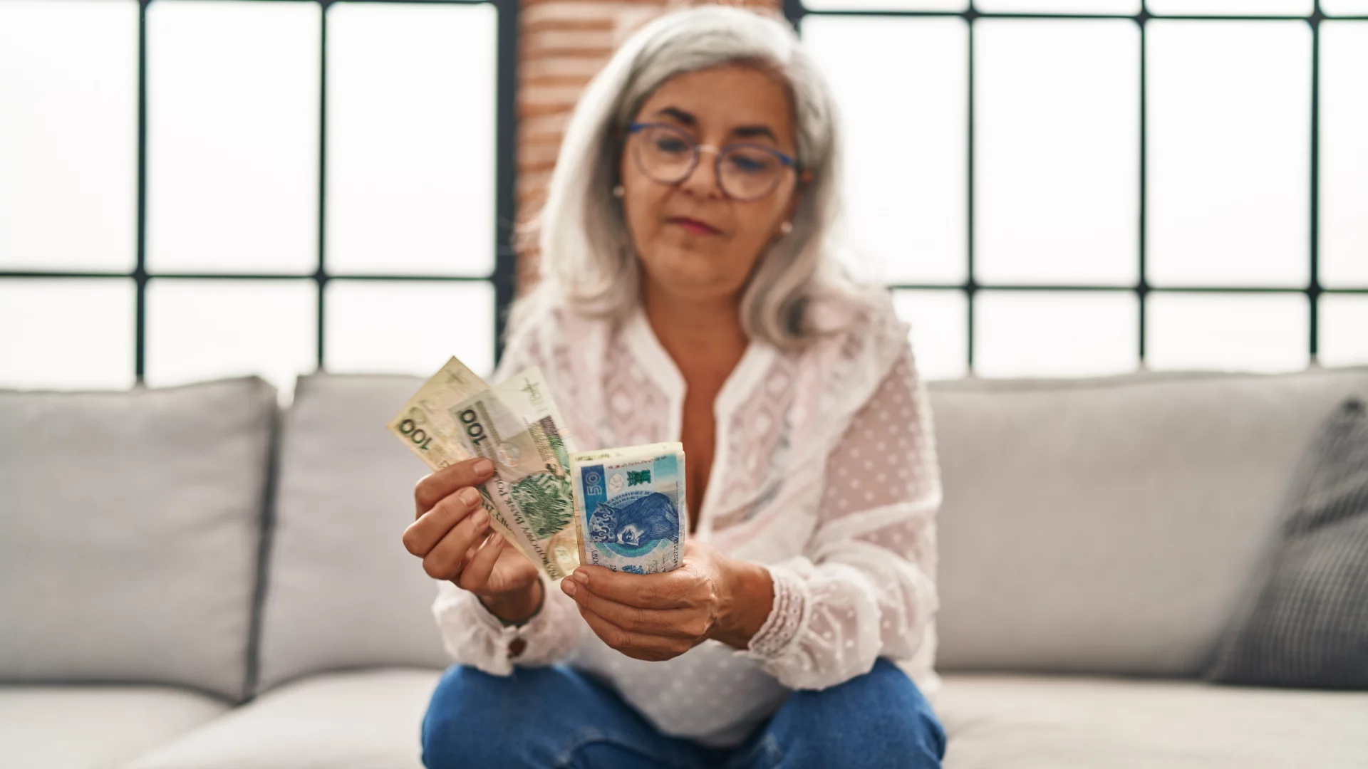 14. emerytura w 2026 roku. ZUS szykuje wypłaty, ale potrąci podatek Seniorka liczy polskie banknoty na kanapie