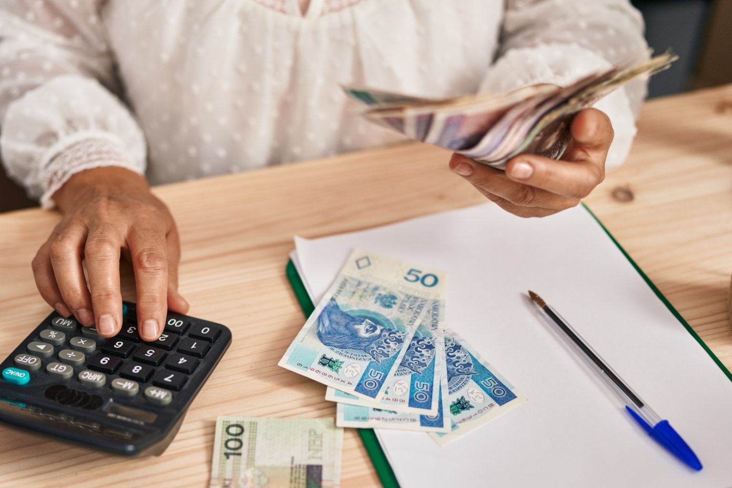 Seniorka przy stole liczy pieniądze z kalkulatorem