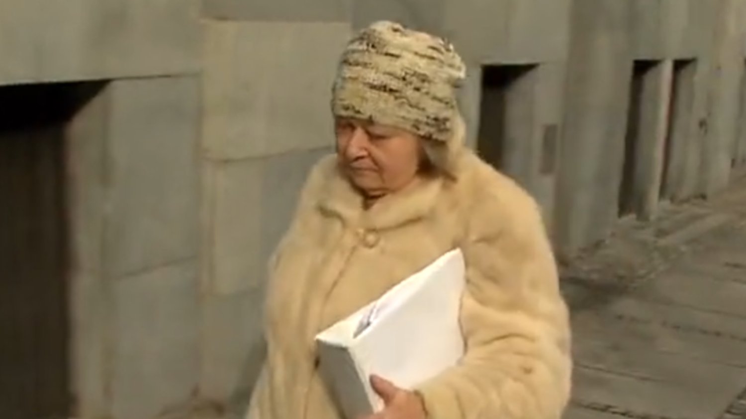 Starsza kobieta w futrze niosąca teczkę
