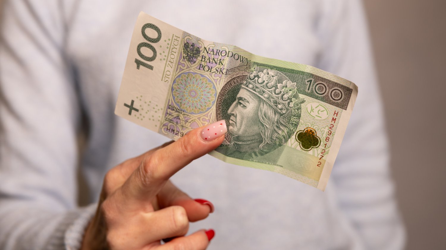 Płaca minimalna 2027: 4950 zł brutto. Ile na rękę? Zbliżenie dłoń trzymającą banknot 100 zł
