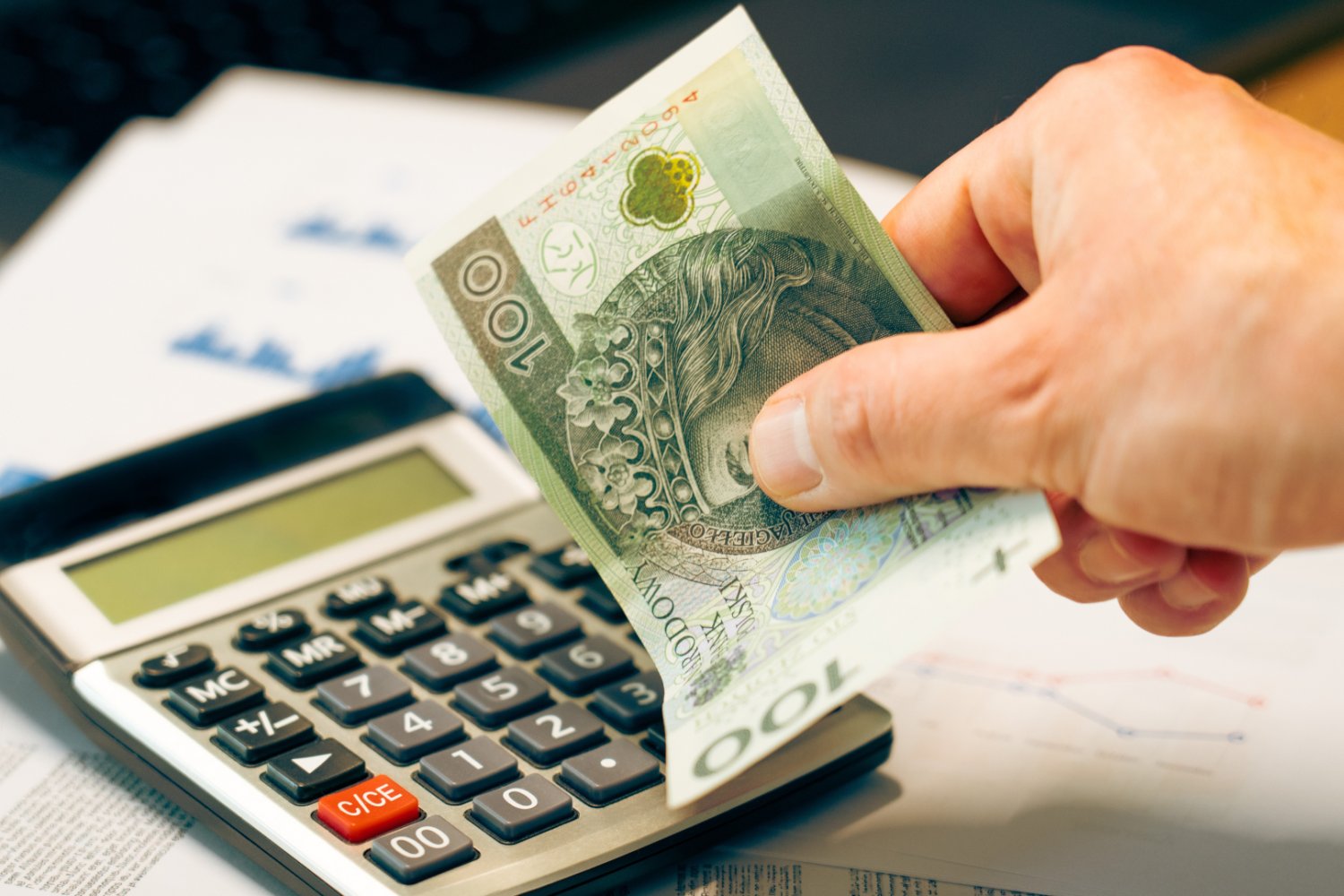Zbliżenie na dłoń przedsiębiorcy z banknotem 100 zł