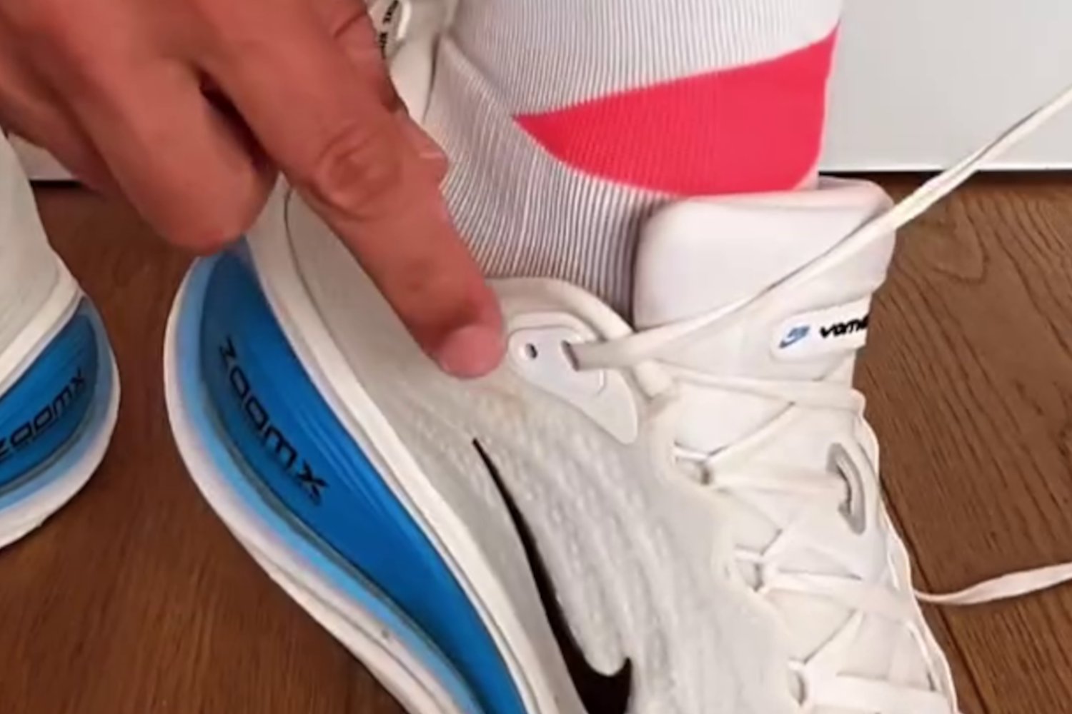 Zbliżenie na sznurowane buty do biegania. Widoczna dodatkowa dziurka w bucie tuż przy kostce wskazywana palcem