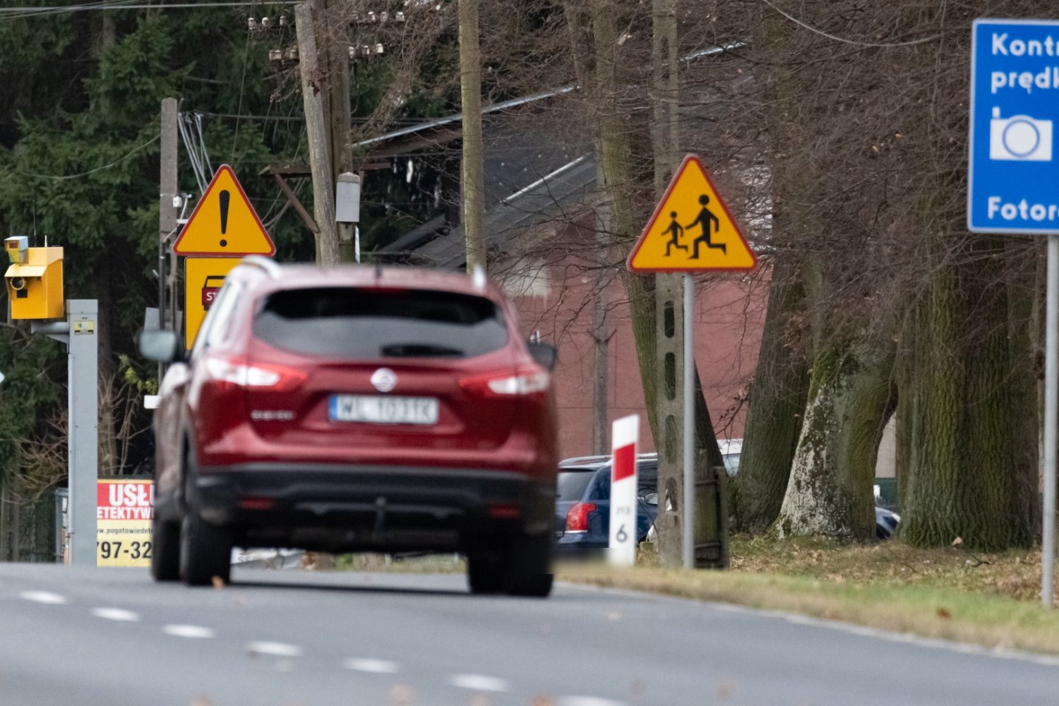 Żółty fotoradar stojący przy polskiej drodze i znak informujący o tym